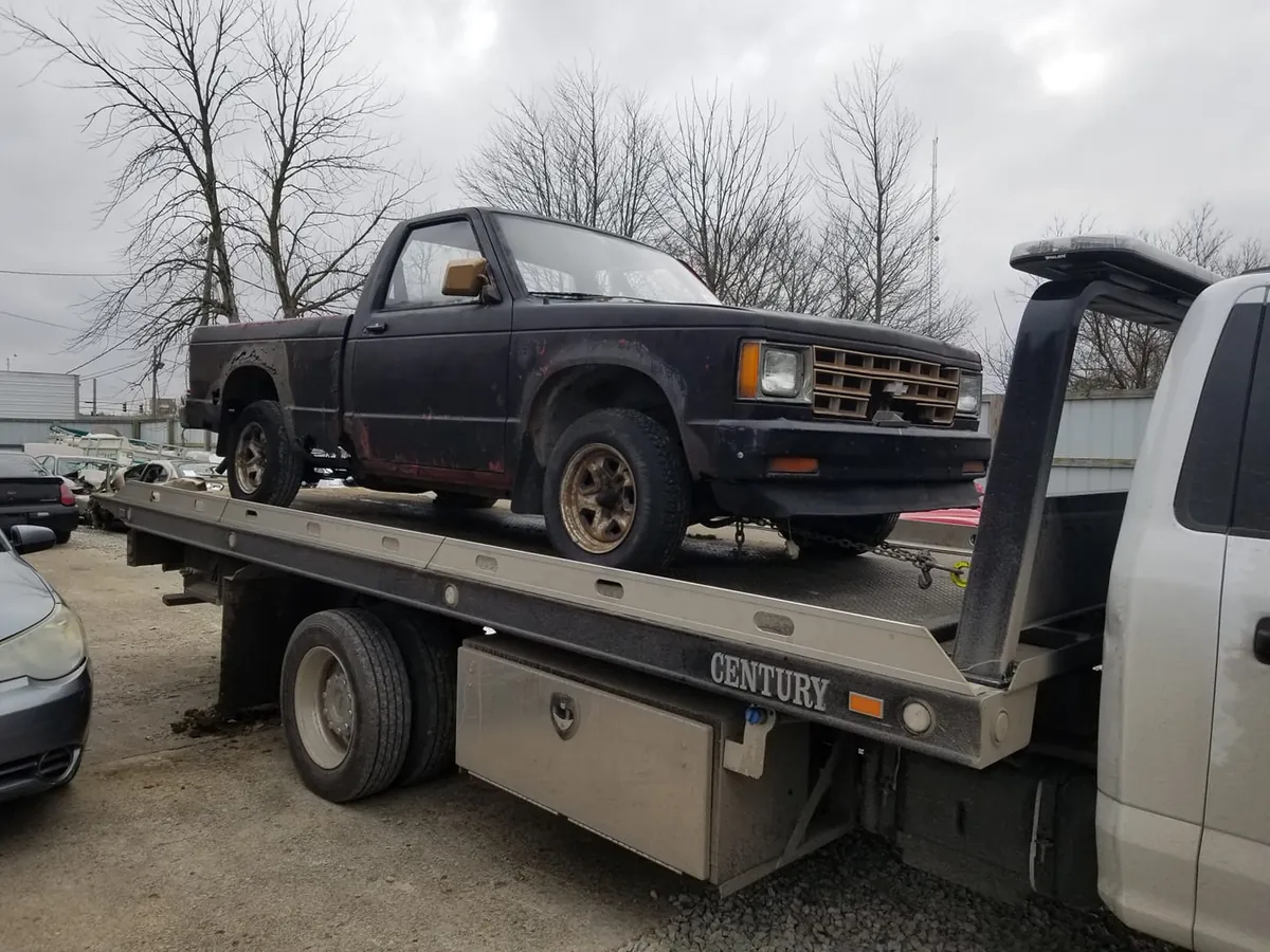 Who buys cars that don't run in Indianapolis: a rusted Chevy S10 pickup secured on a flatbed tow truck for a cash pickup