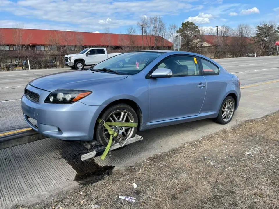 A light blue Scion tC with a visible fluid leak being towed along an Indianapolis highway -- leaking or not, the parts keep their value