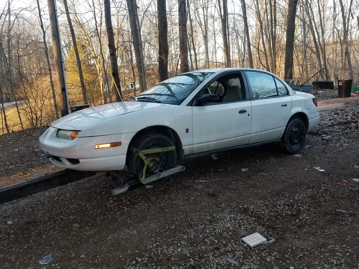Dusty white Saturn SL photographed in a gravel lot before quote calls -- daylight photos keep the phone offer honest