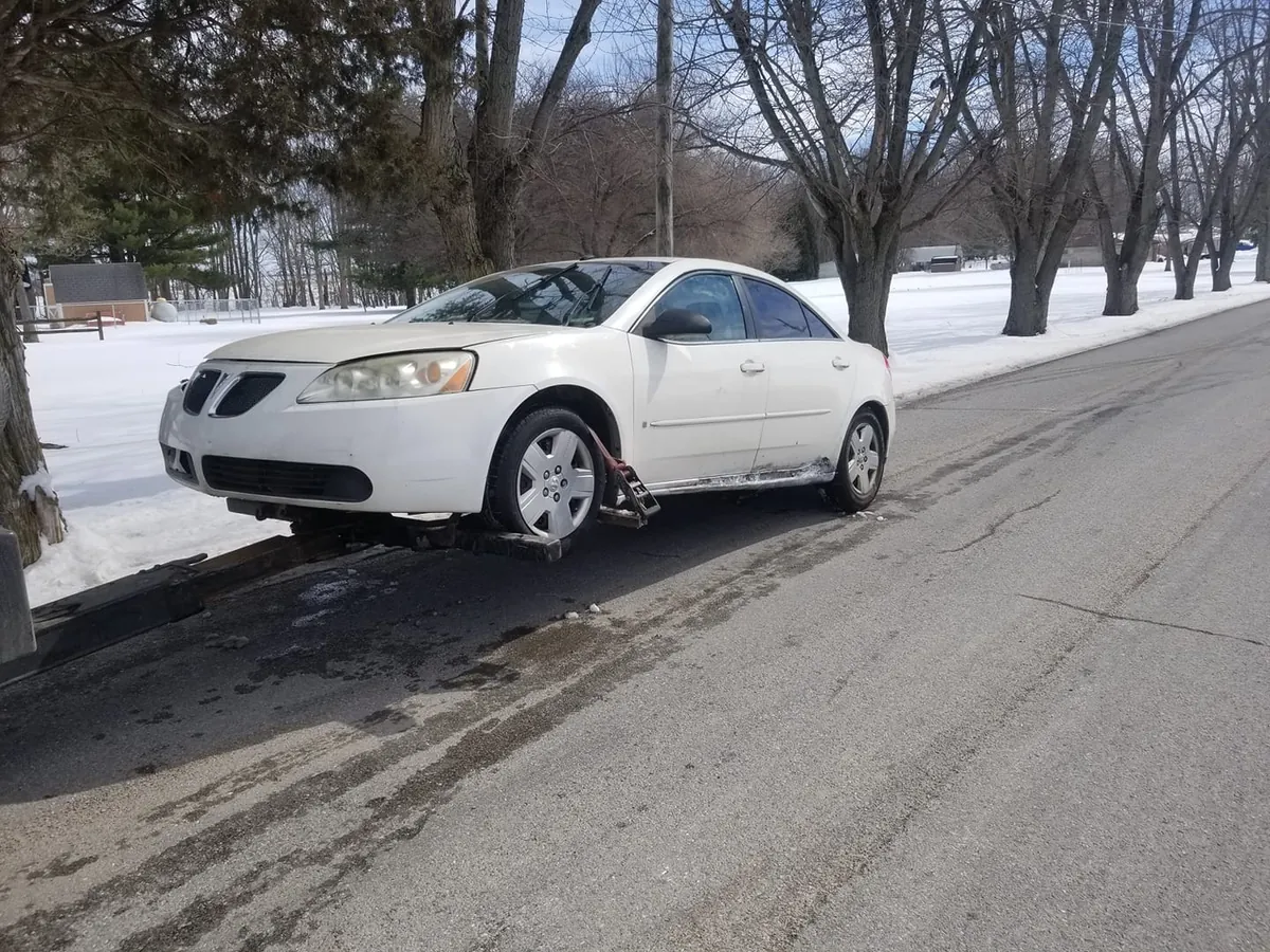 Non-running Pontiac G6 loaded for towing on a snowy street, proof that junk car pickup in Indianapolis runs all winter