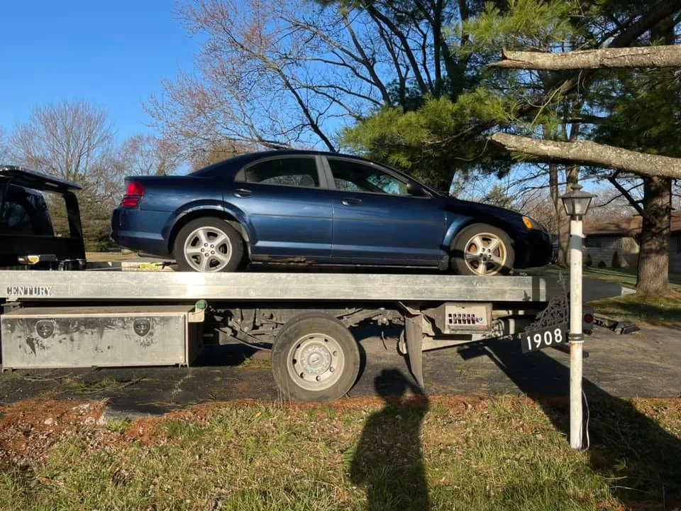 Free junk car removal in Indianapolis: an older sedan loaded onto a flatbed tow truck at a local home