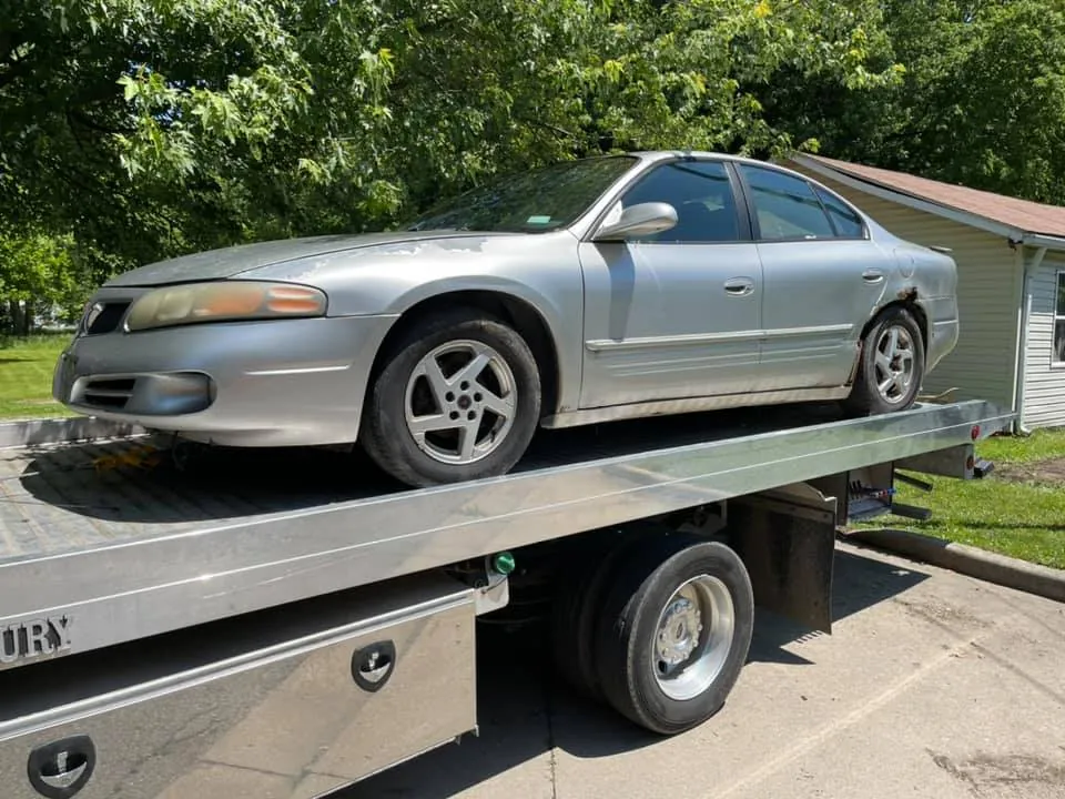Silver Pontiac Grand Prix being loaded onto a flatbed in an Indianapolis residential setting, an older vehicle that may qualify for Indiana's Certificate of Authority