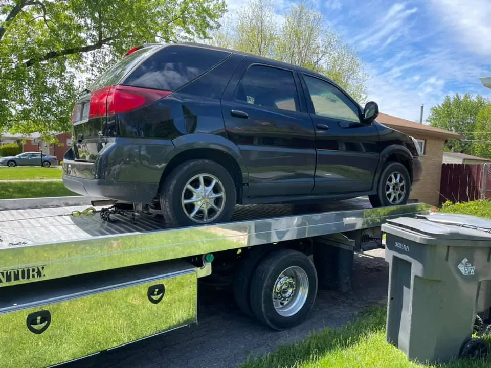 An older black Buick Rendezvous that looks trade-in ready heads out on a flatbed -- its owner took cash instead of a token dealer allowance