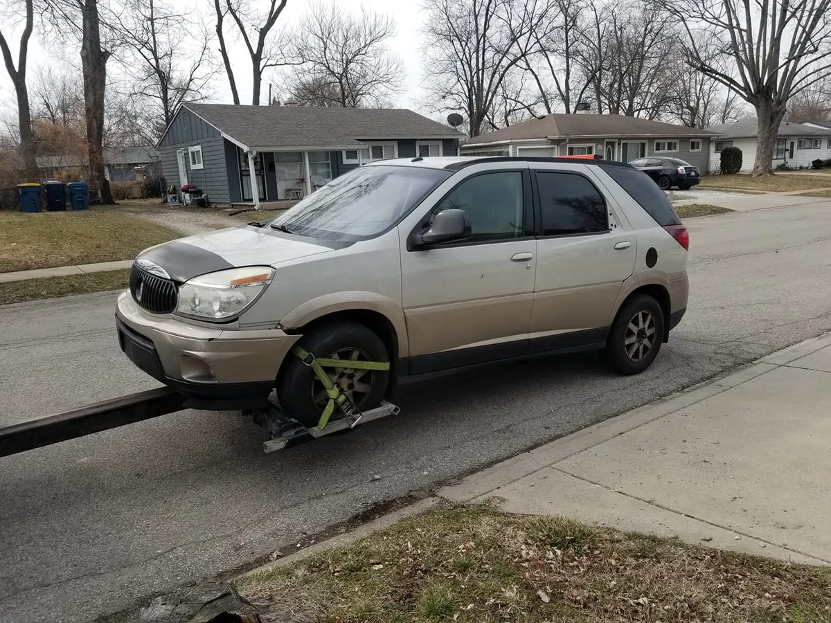 Buick Rendezvous with front bumper damage being towed at no charge on an Indianapolis residential street